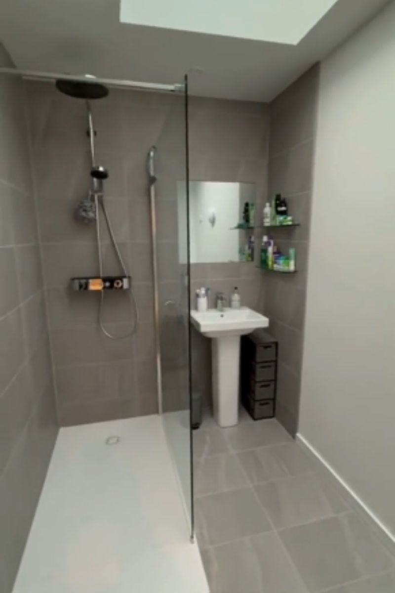 A fully tiled shower room with sink, storage shelves and a skylight