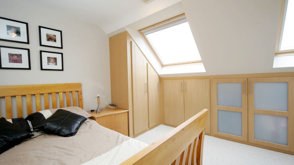 A spacious bedroom with modern light timber storage furniture and two VELUX windows